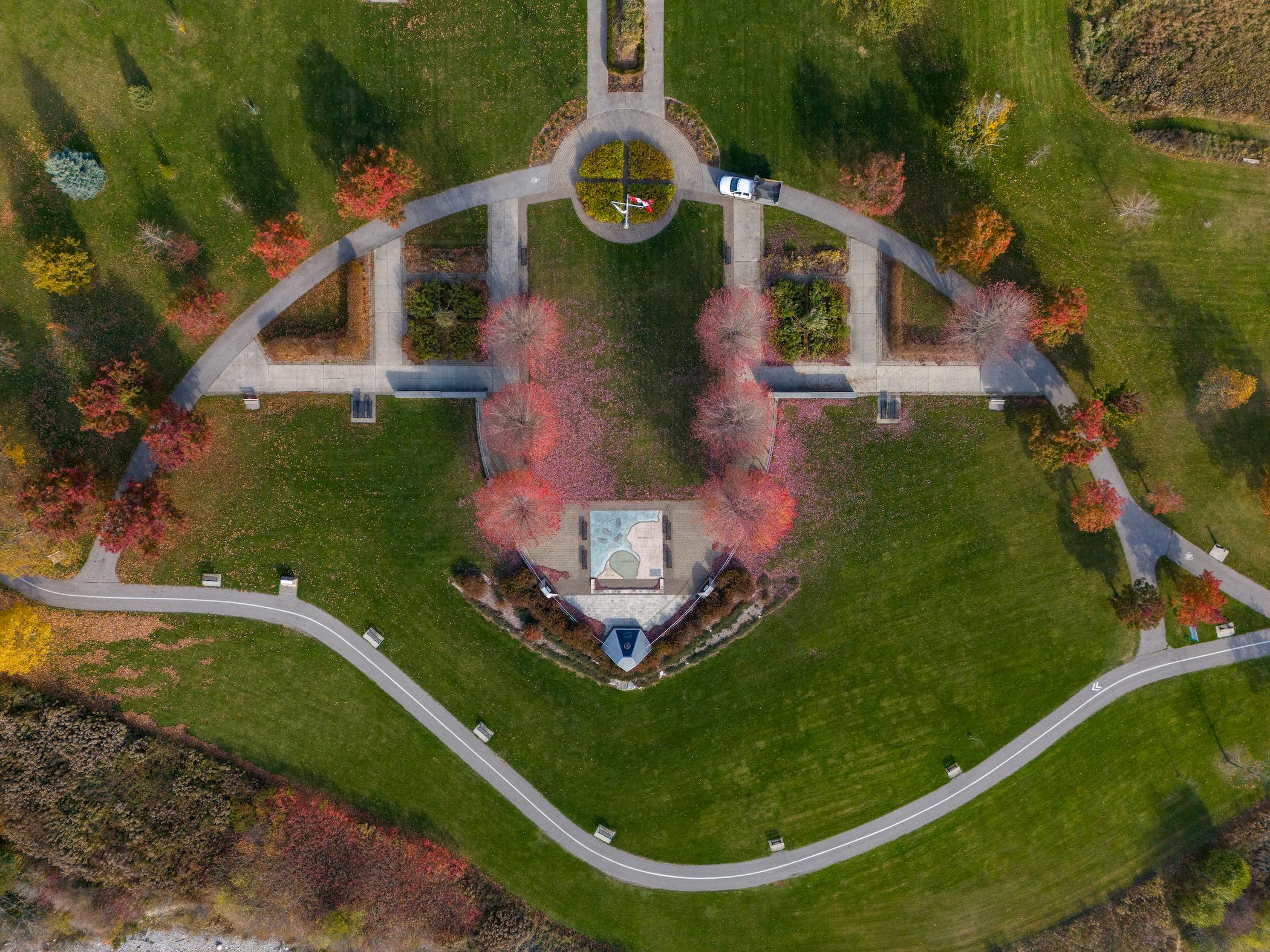 Aerial view of a landscaped park with a central memorial, curved footpaths, and autumn trees.
