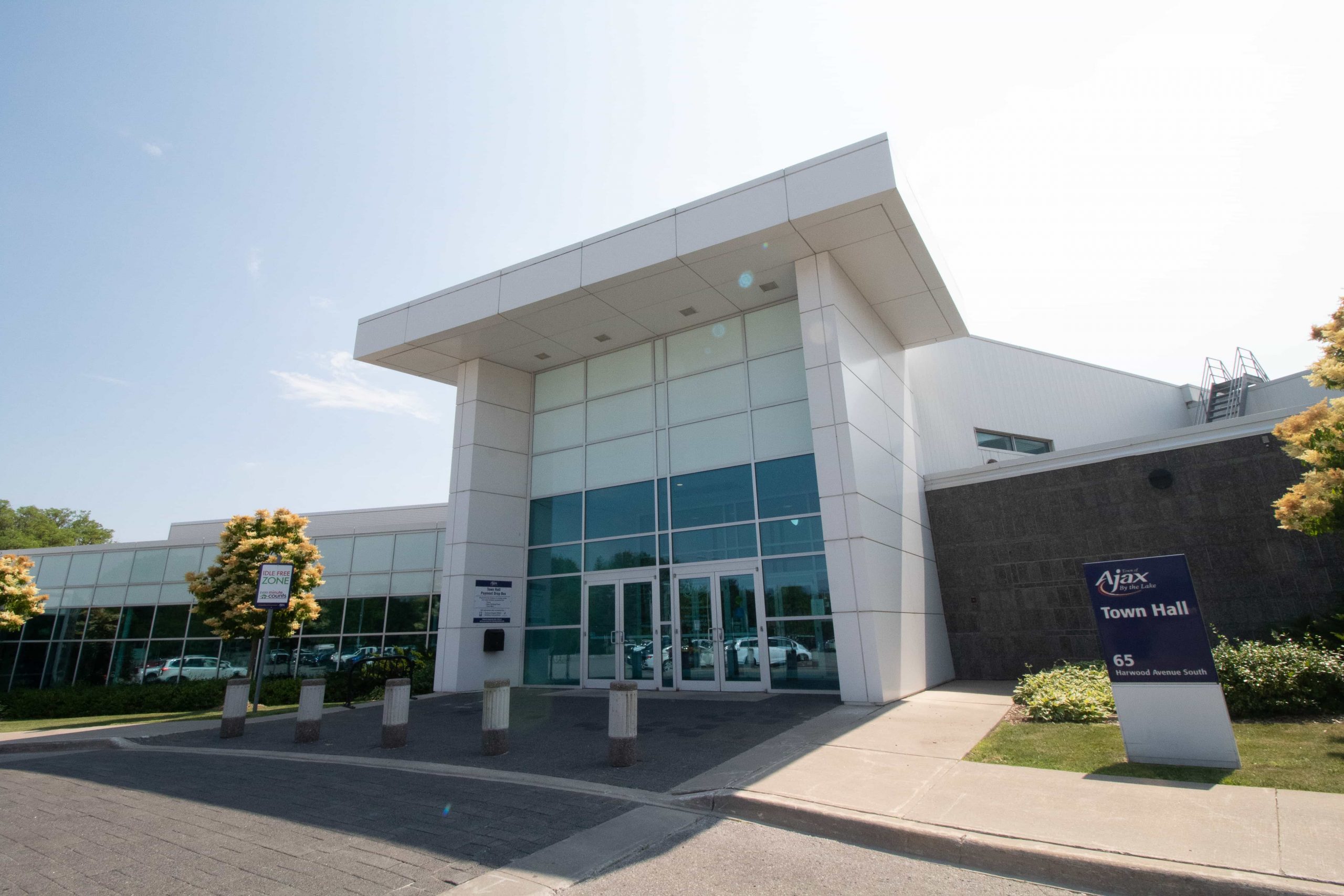 Front entrance of a modern building with glass doors, labelled "Ajax Town Hall" on a sign near the pavement.