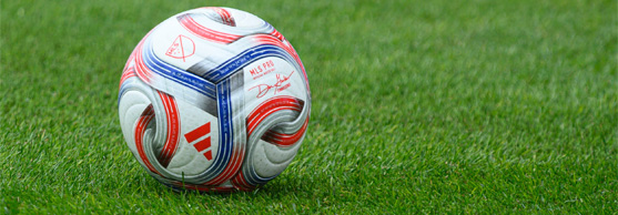 A white football with red and blue patterns rests on green grass.