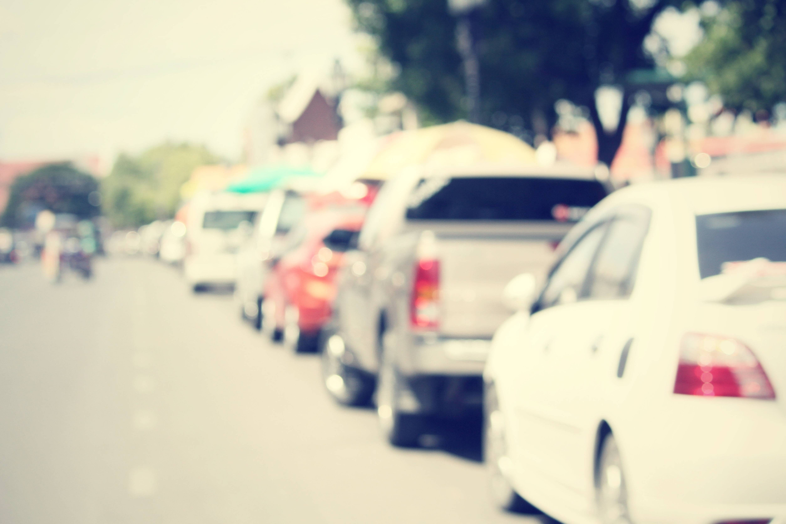 Row of cars parked along a street in daylight, with the image appearing blurred and out of focus.