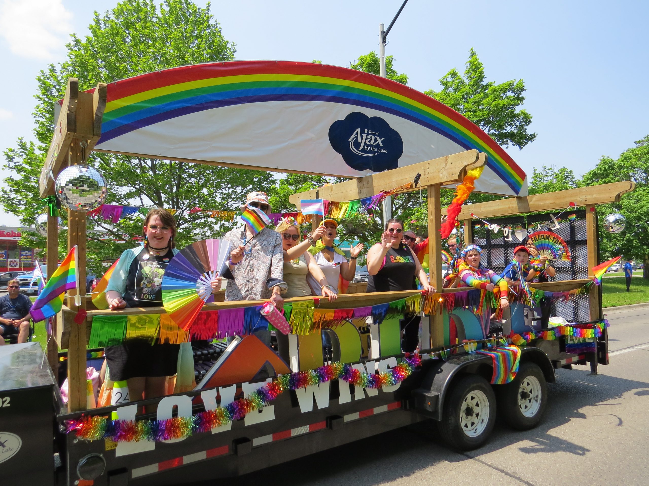 A parade float with a rainbow canopy, disco balls, and people waving flags, decorated with "LOVE WINS".