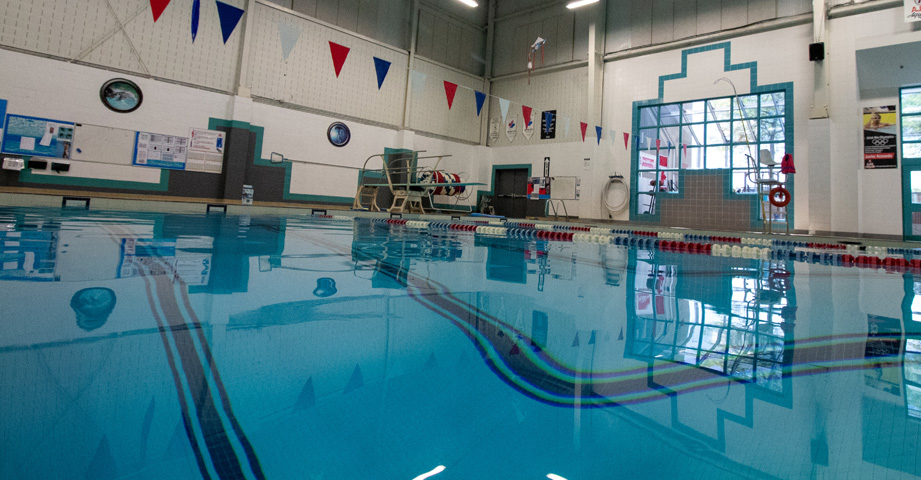 Indoor swimming pool with lane dividers, lifeguard chair, and flags hanging above in a brightly lit facility.