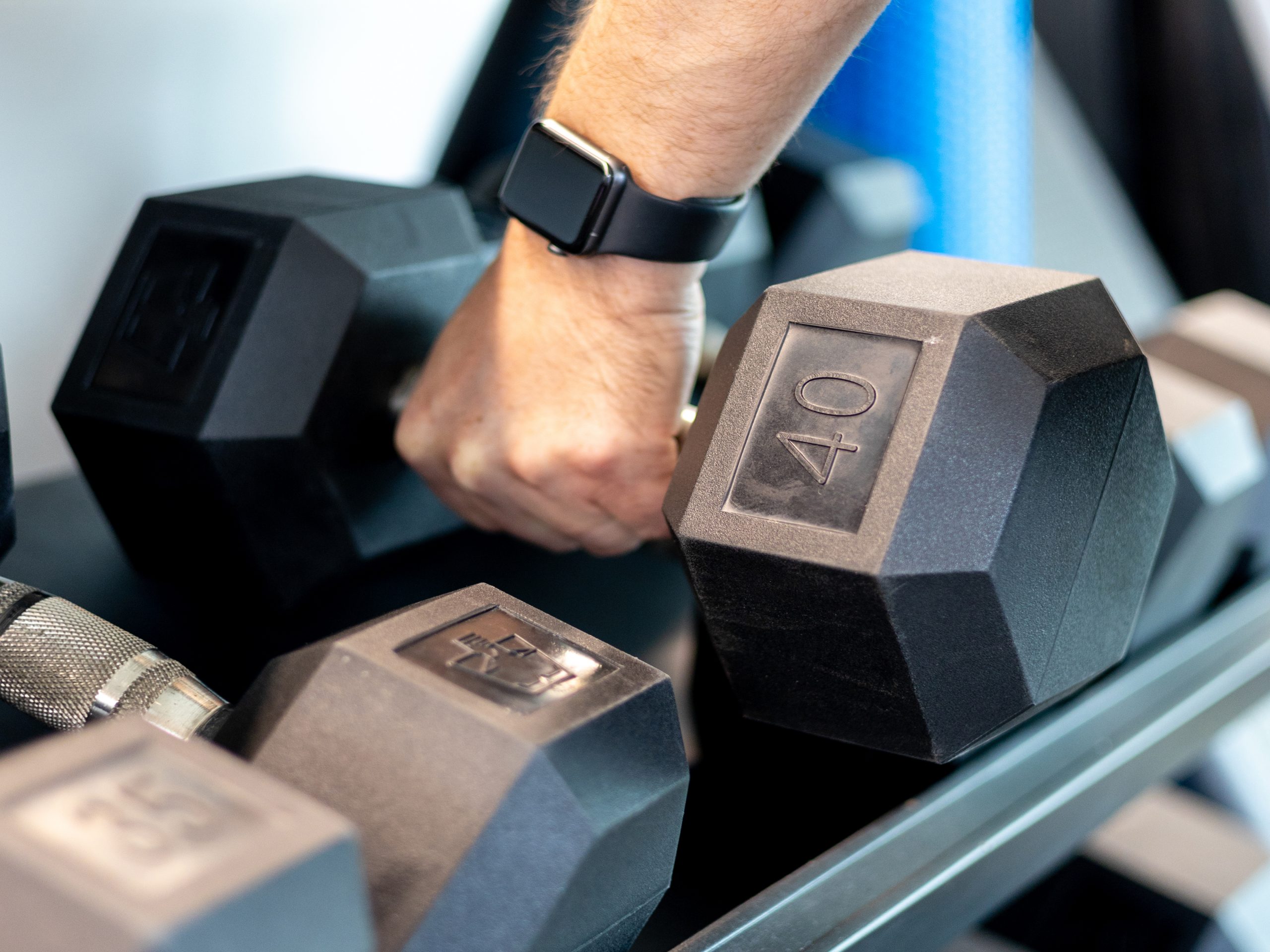 A person wearing a smartwatch lifts a 40-pound dumbbell from a rack with other weights.