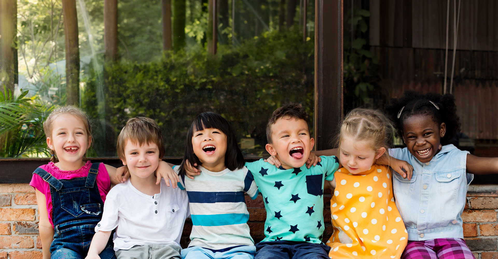 A group of smiling children sit on a bench together.