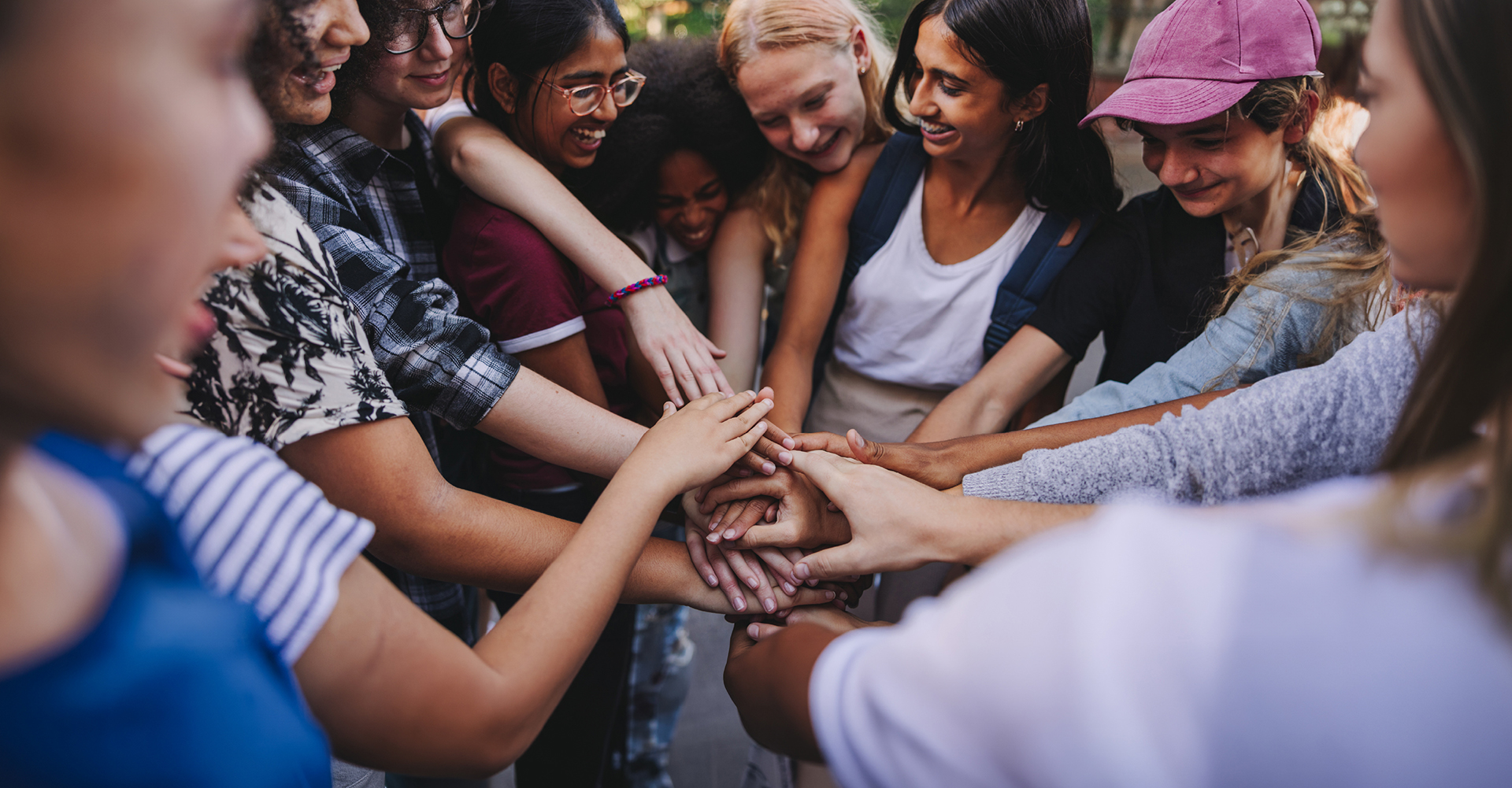 A group of people stand in a circle outdoors, stacking their hands together in the centre.