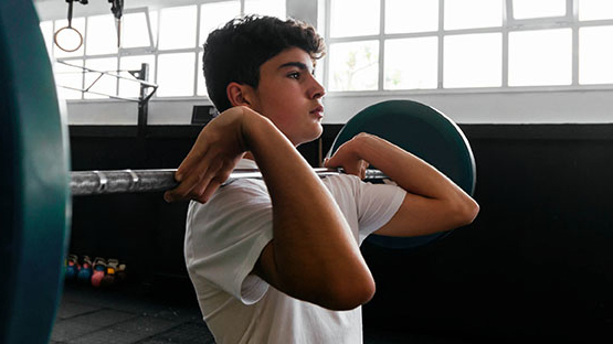 Teen lifts a barbell above his chest.