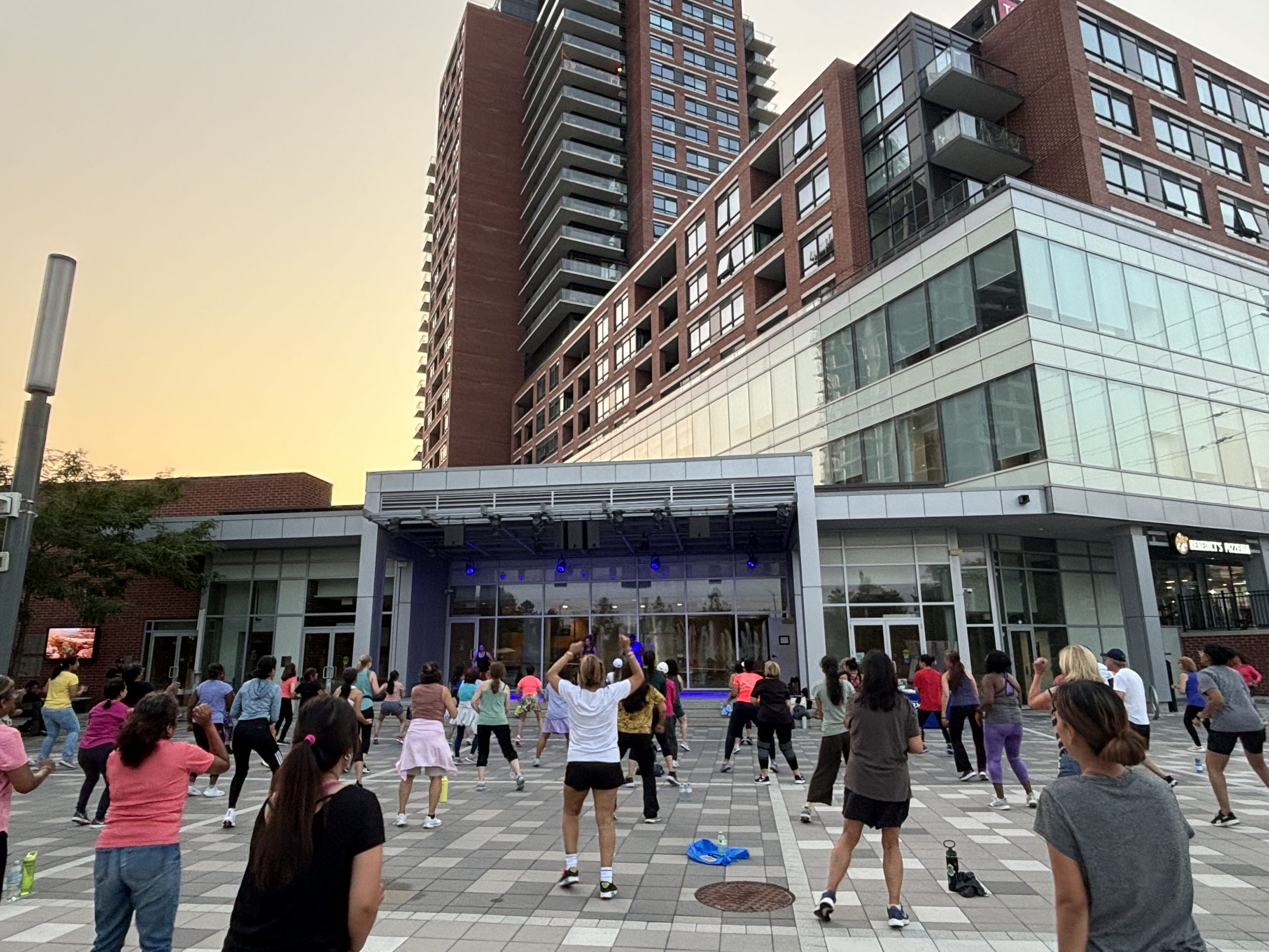 A group of people participate in an outdoor fitness class in front of a modern building at sunset.