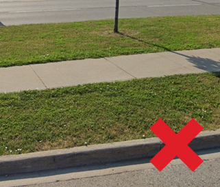 A pavement with a grassy verge beside a road; a red X is marked on the grass near the kerb.