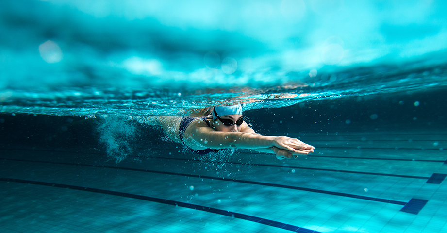 A person swims underwater in a pool, wearing goggles and a swimming costume, with arms outstretched in a streamlined position.