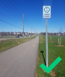 Paved path with a "Shared Path" sign beside a road under clear blue sky; green tick in corner.