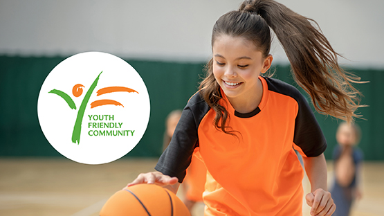 Girl in orange sports kit dribbling a basketball indoors, with a "Youth Friendly Community" logo beside her.