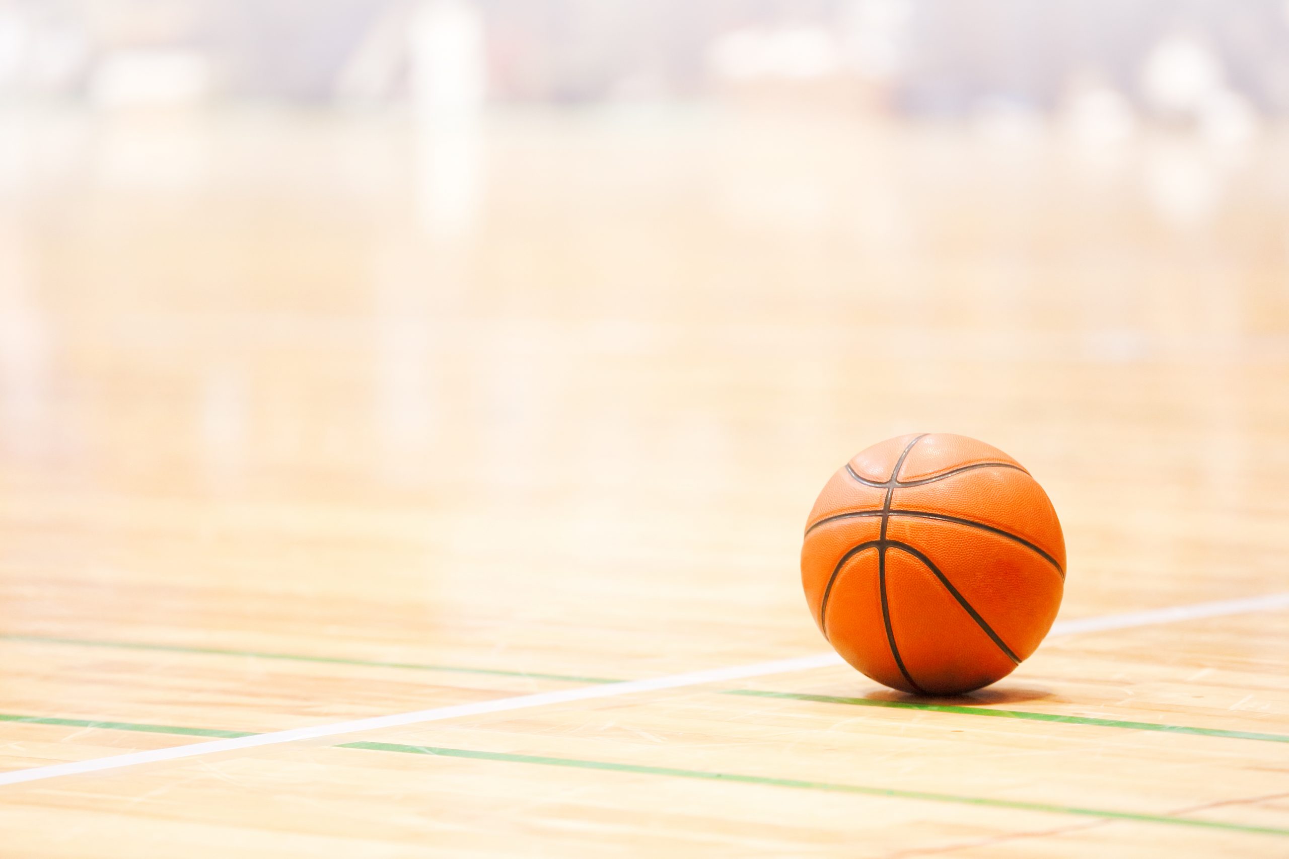 A basketball rests on a polished indoor court with blurred lines and background.