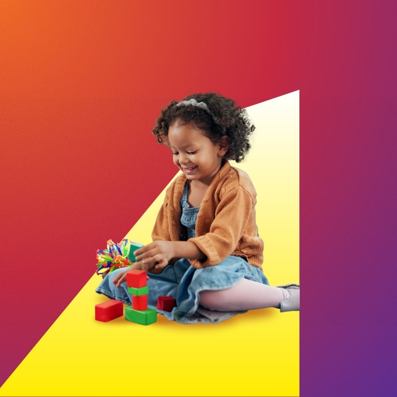 A young child sits on the floor playing with building blocks.
