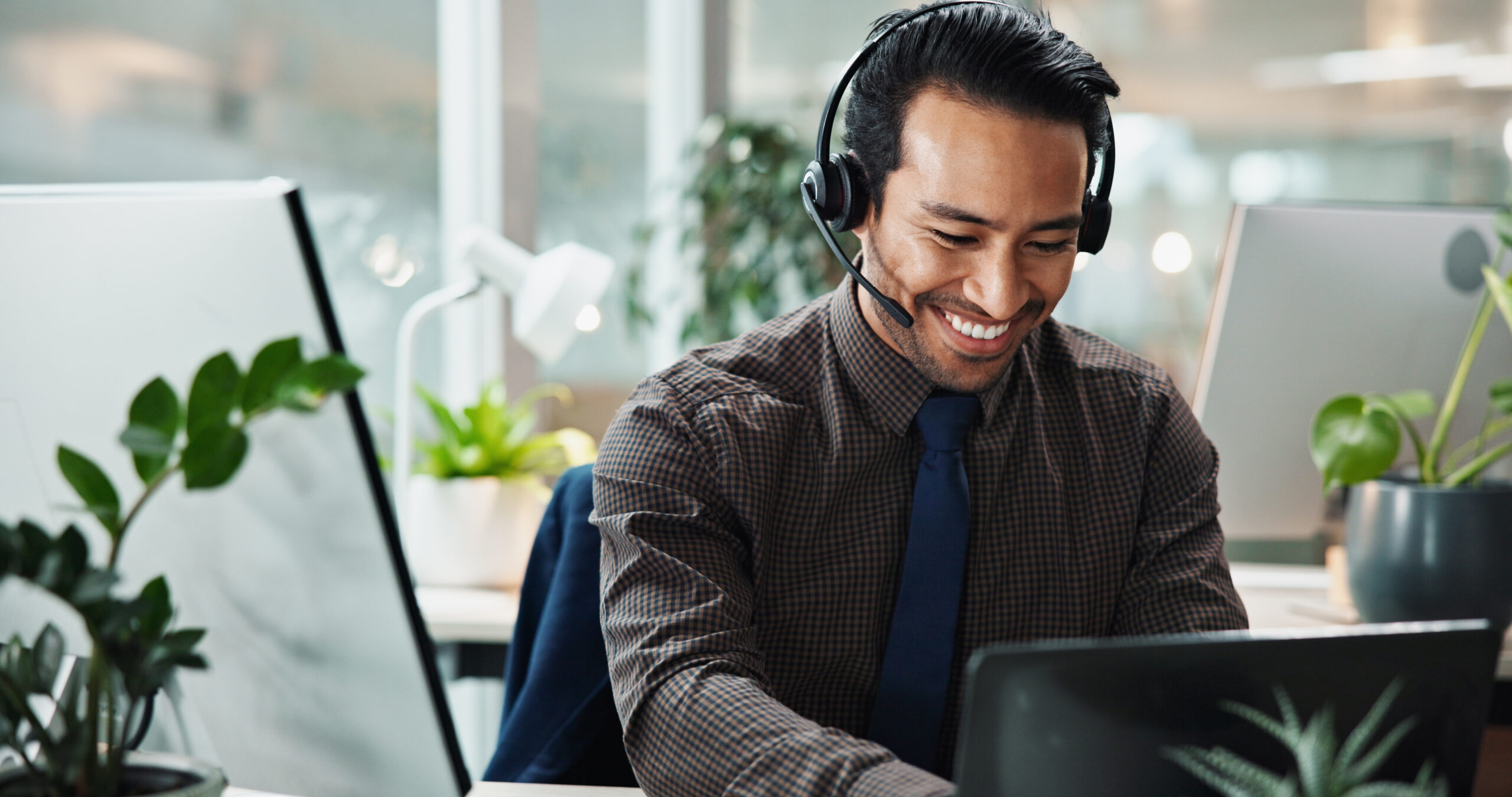 A customer service representative wearing a head set smiles at his computer.